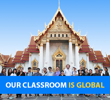 Our Classroom Is Global. Photo shows Visioneers Daniel Kish and Brian Bushway standing with blind student coaches in front of a temple in Thailand.