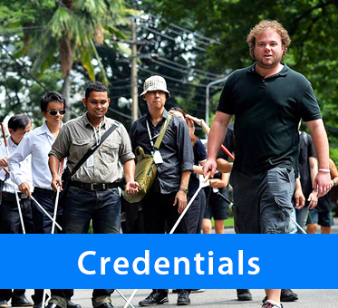 Photo: Brian Bushway leading a group of blind coach trainees along a street in Bangkok, Thailand. Caption: Credentials.