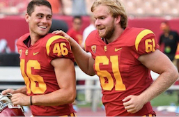 Photo of Jake Olson, 18 year-old long snapper for the USC Trojans runs with his hand on the shoulder of a team mate after snapping for the winning point in a game.