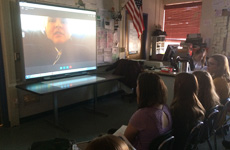 Visioneer J. Steel-Louchart is pictured on a large video screen interacting with a Science class of students via Skype.