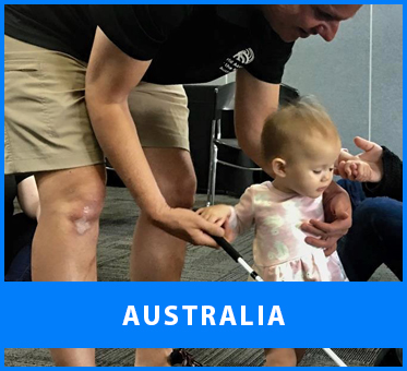 Australia. Image: Daniel Kish works with a toddler while helping her to walk using a Perception Cane at a workshop in Australia.