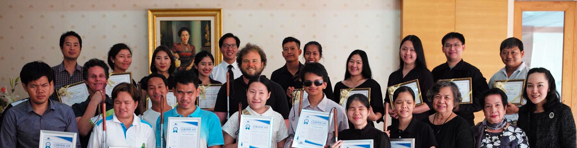 Image: Lead Visioneer Daniel Kish, Senior Visioneer Brian Bushway and Workshop Visioneer Thomas Tajo stand for a group photo with staff and blind coaching students at the Foundation for the Blind in Thailand. The student coaches are holding their framed Instructor Level Certificates.