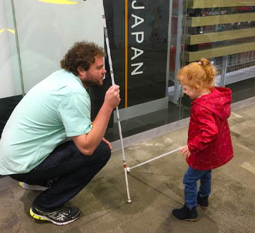 Senior Instructor Visioneer crouches down to work with a young Student Visioneer at a mall in Australia.