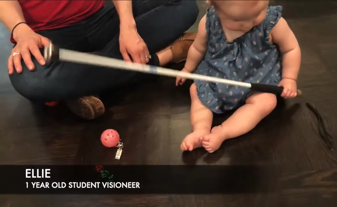 Video still of one-year-old Ellie getting a grip on a cane while sitting on the floor.